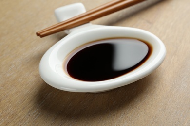 Photo of Dish of soy sauce with chopsticks on wooden background, closeup