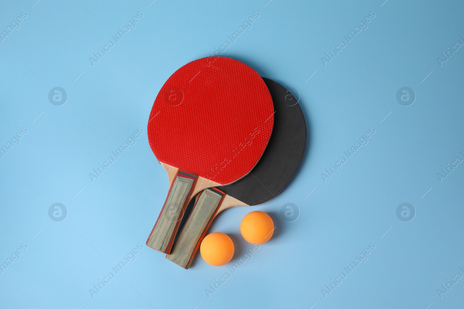 Photo of Ping pong balls and rackets on light blue background, flat lay