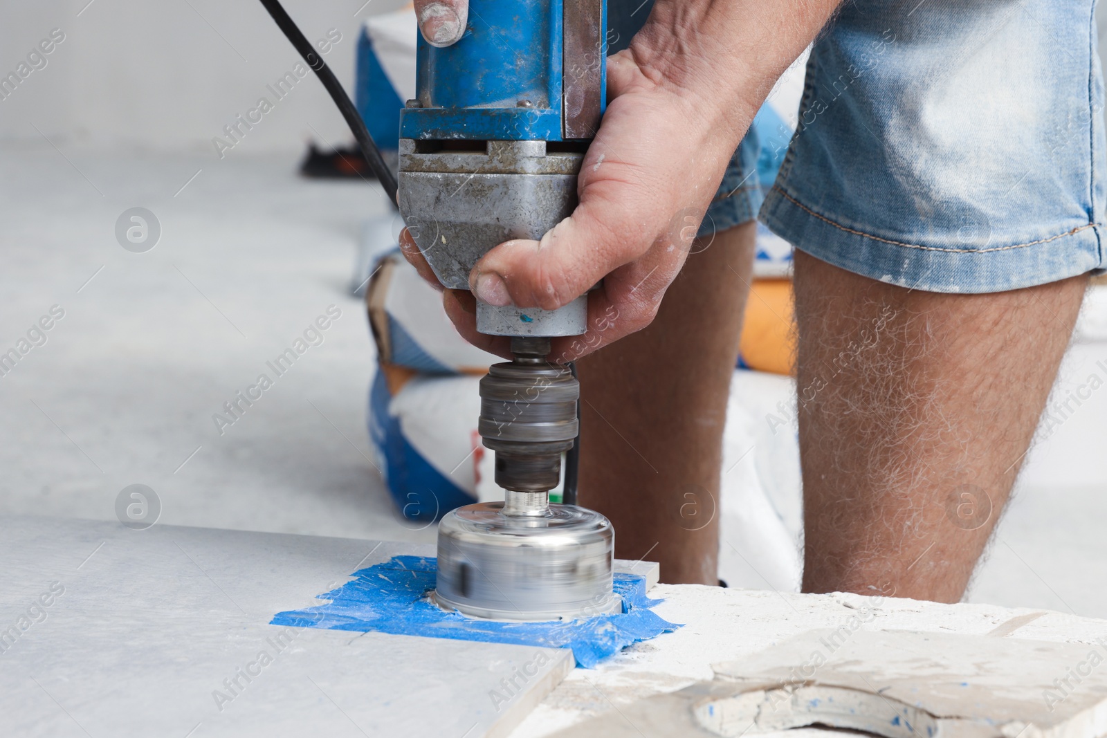 Photo of Worker with electric drill preparing tiles for installation indoors, closeup