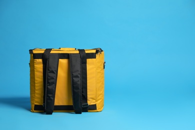 Photo of Modern yellow thermo bag on light blue background. Space for text
