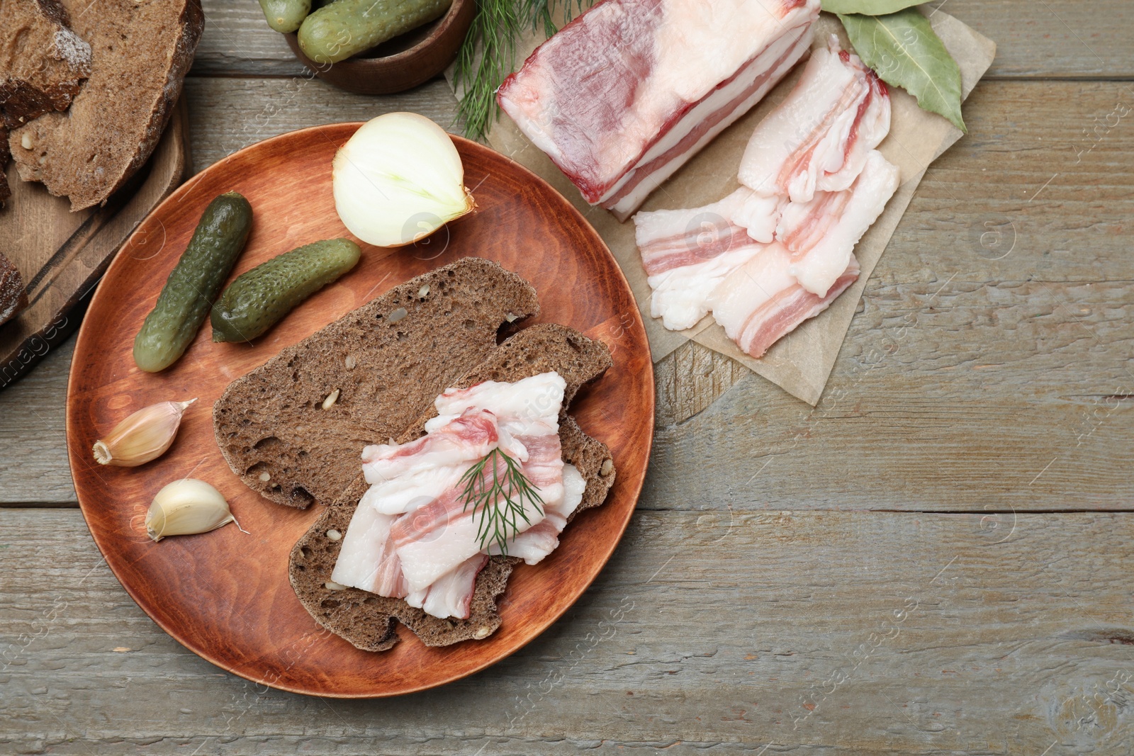Photo of Tasty salt pork with rye bread, pickled cucumbers and dill on wooden table, flat lay
