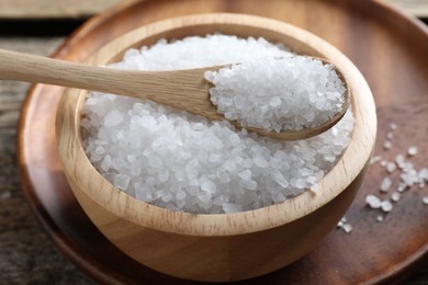 Photo of Organic salt in bowl and spoon on wooden table, closeup