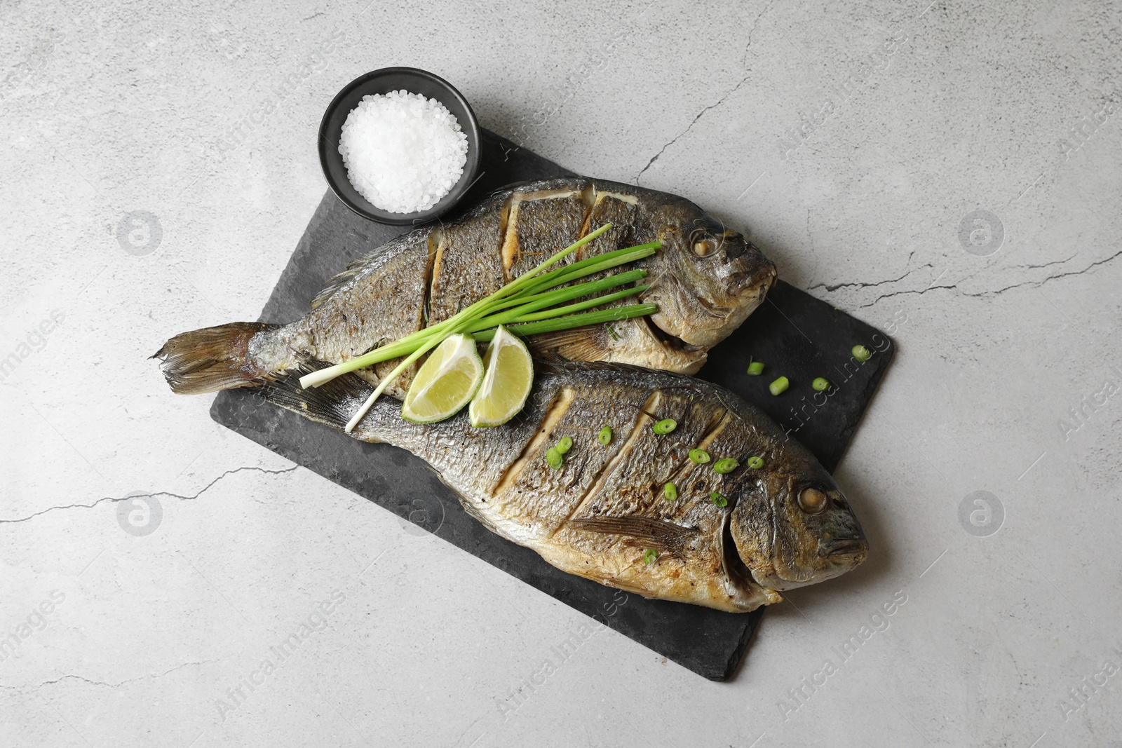 Photo of Seafood. Delicious baked fish served with green onion and lime on light textured table, top view