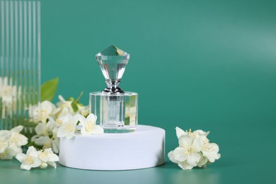 Photo of Presentation of aromatic perfume in bottle and beautiful jasmine flowers on green background, space for text