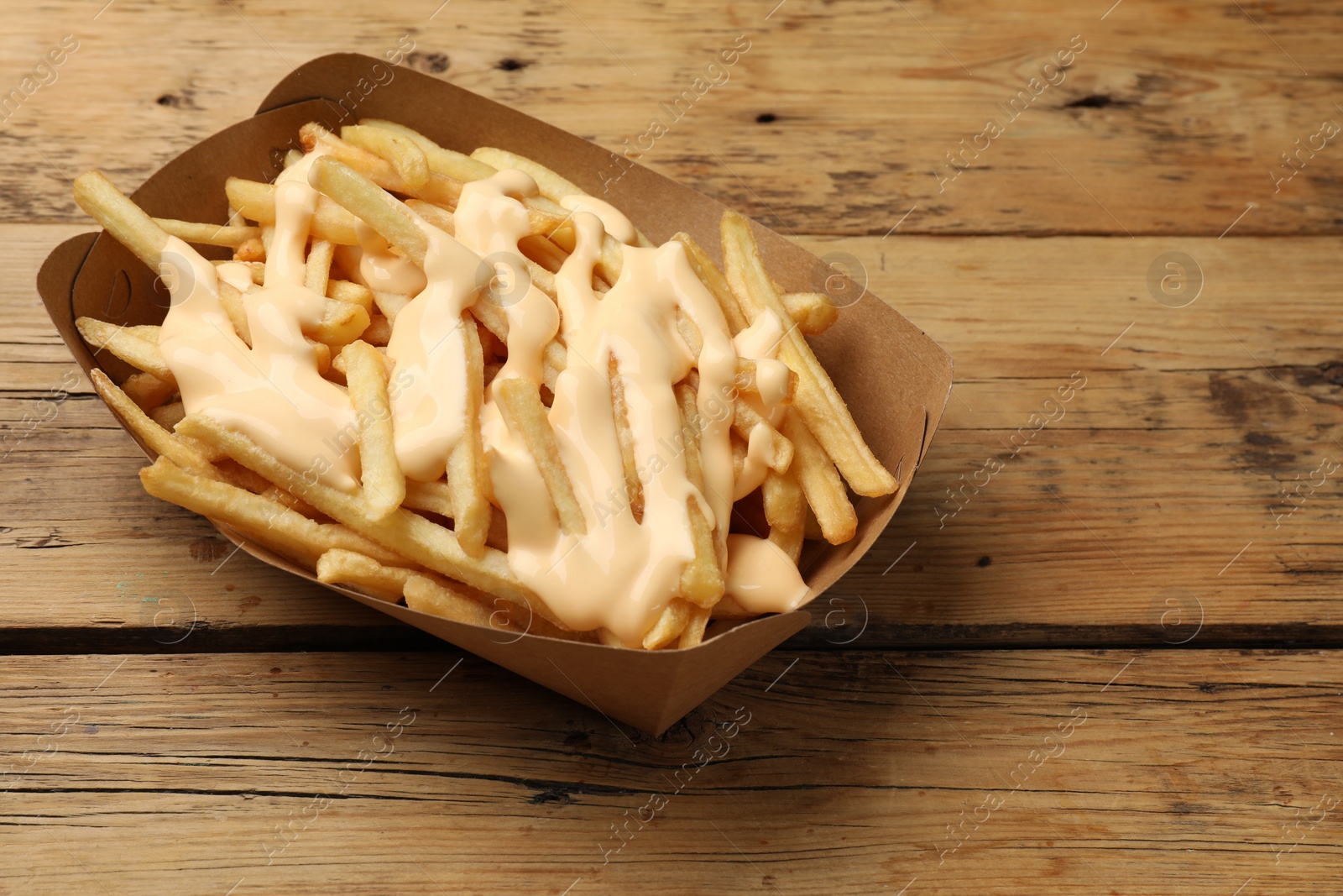 Photo of Delicious French fries with cheese sauce on wooden table, closeup