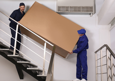 Professional workers carrying refrigerator on stairs indoors