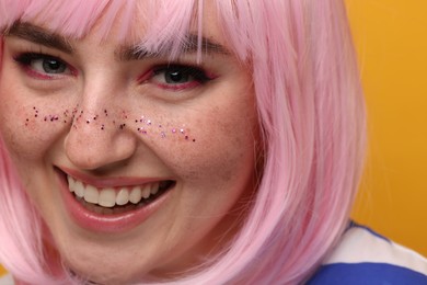 Smiling woman with bright makeup and glitter freckles on yellow background, closeup