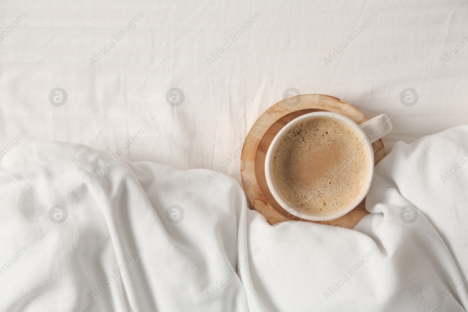 Photo of Cup of aromatic coffee on bed with soft blanket, top view. Space for text