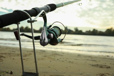 Photo of Fishing rod with reel at riverside, closeup. Space for text
