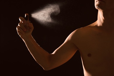 Photo of Young man spraying perfume on black background, closeup