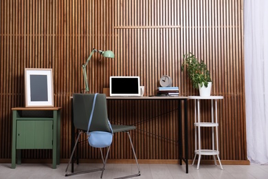 Photo of Stylish workplace interior with laptop on table near wooden wall. Space for text