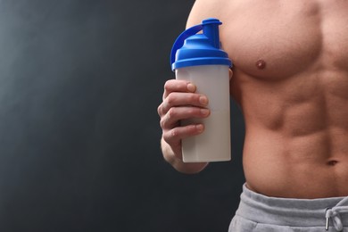 Photo of Young man with muscular body holding shaker of protein on dark grey background, closeup. Space for text