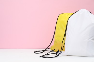 Photo of Two drawstring bags on white wooden table against pink background. Space for text