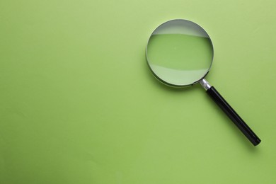Photo of Magnifying glass on green background, top view. Space for text