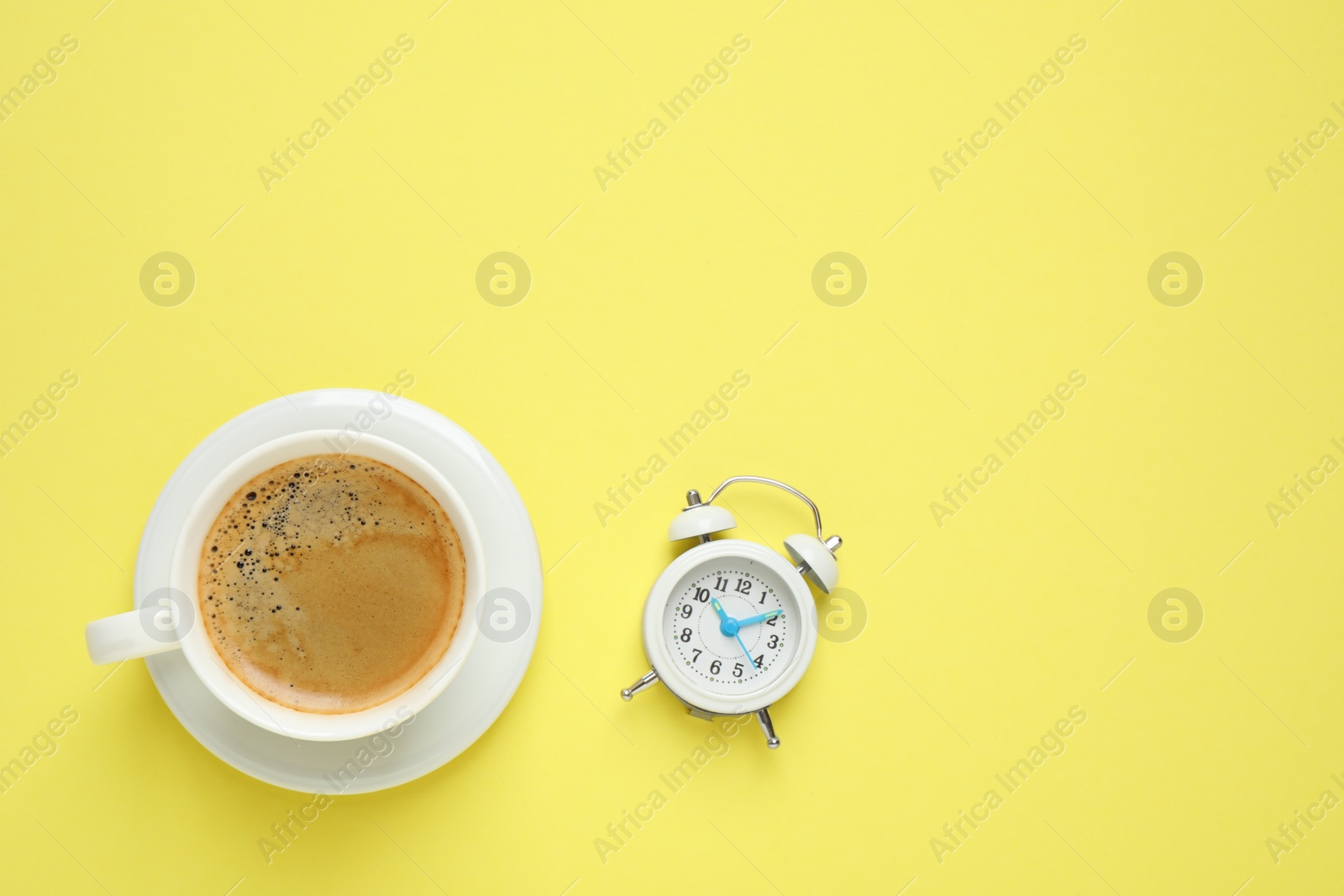 Photo of Cup of morning coffee and alarm clock on yellow background, flat lay. Space for text