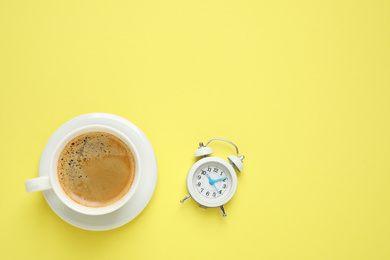 Photo of Cup of morning coffee and alarm clock on yellow background, flat lay. Space for text