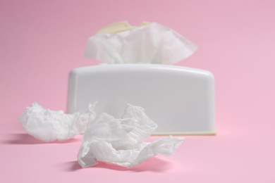 Photo of Holder with paper tissues and used crumpled napkins on pink background