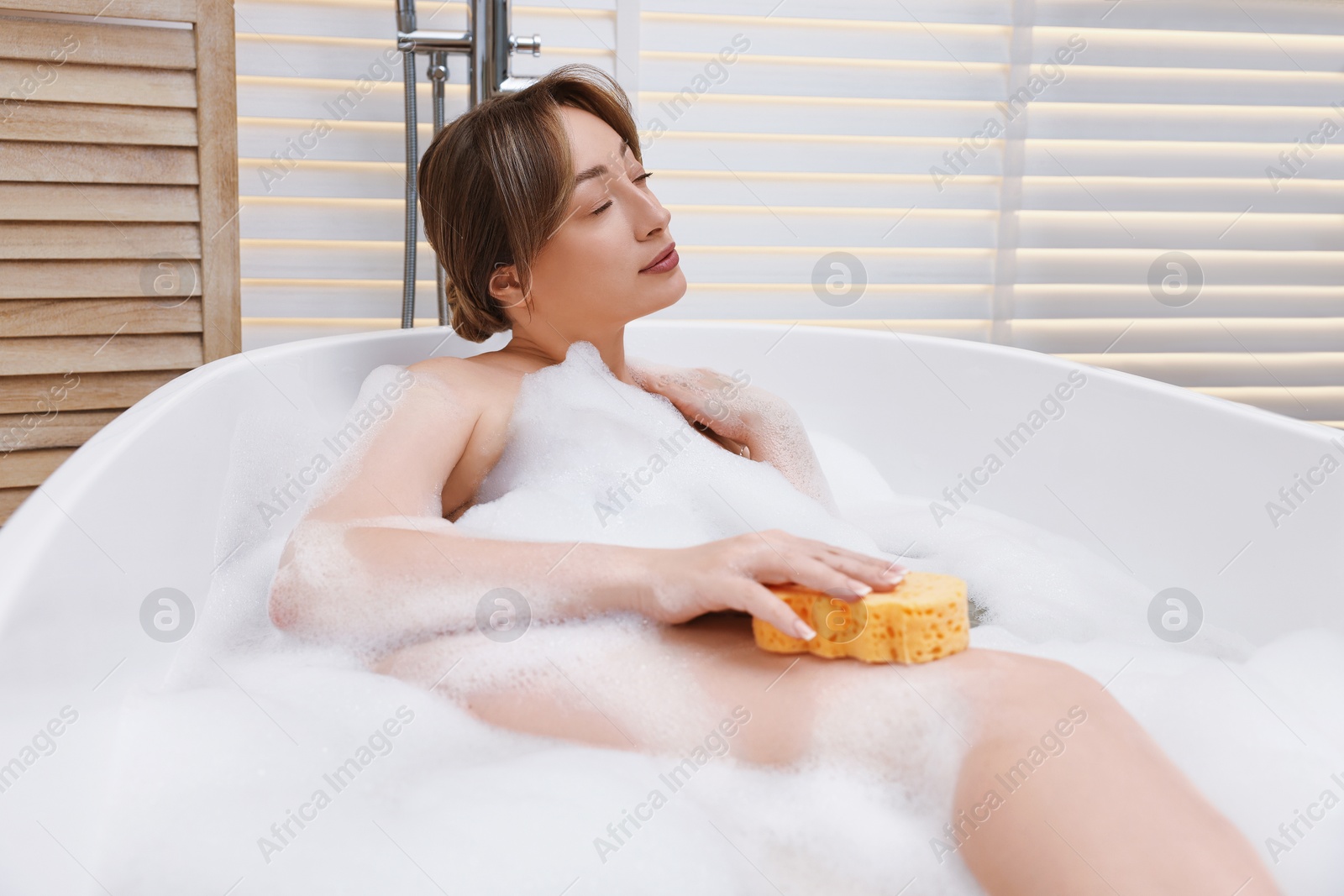 Photo of Beautiful woman taking bath with foam in tub indoors