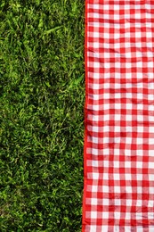 Photo of Checkered picnic tablecloth on fresh green grass, top view. Space for text