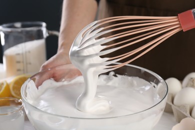 Photo of Woman making whipped cream with whisk at table, closeup