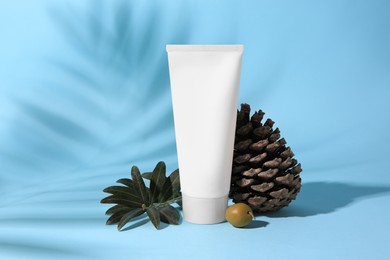 Photo of Tubecream, olive and cone on light blue background. Cosmetic products