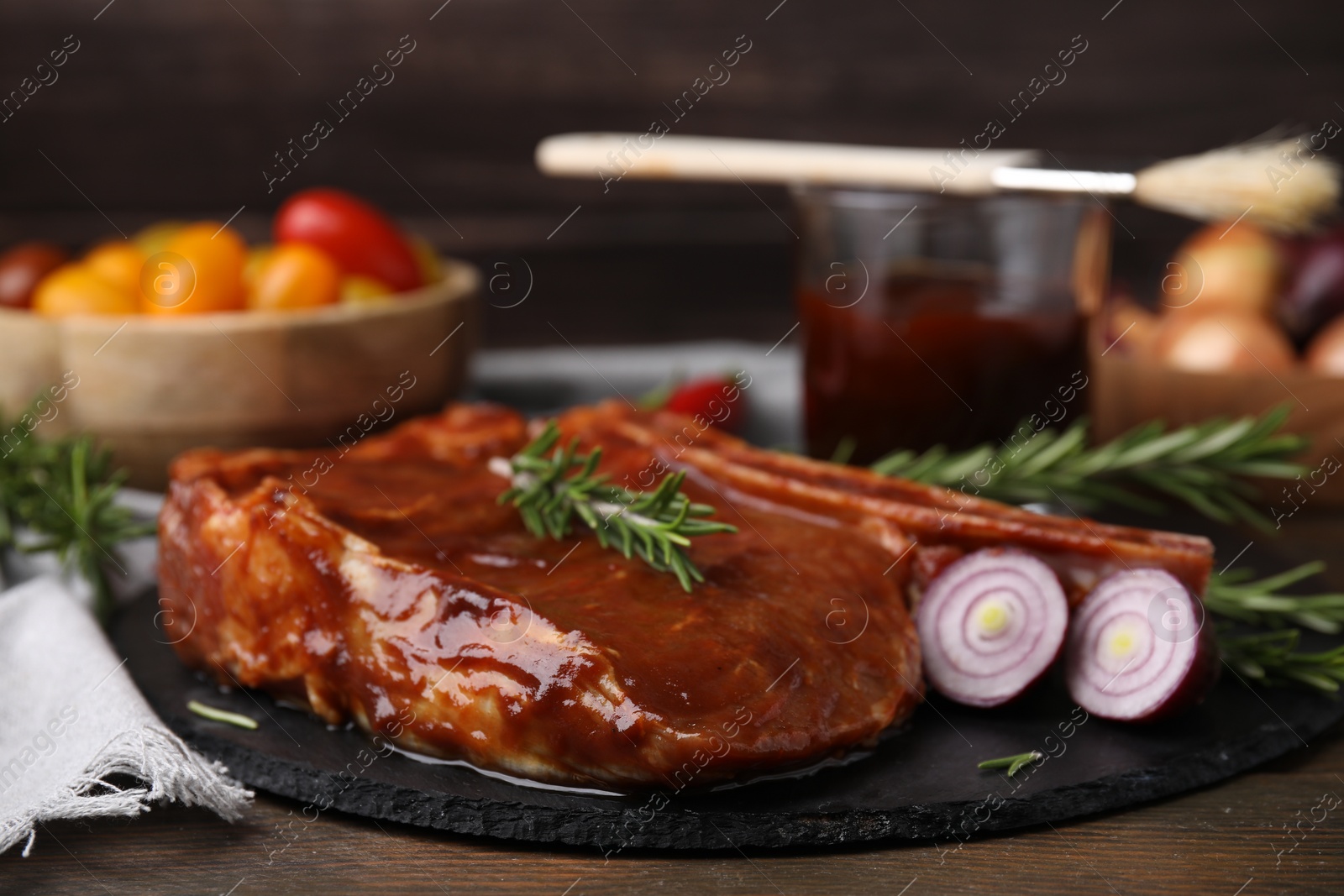 Photo of Tasty marinated meat, rosemary and onion on wooden table, closeup
