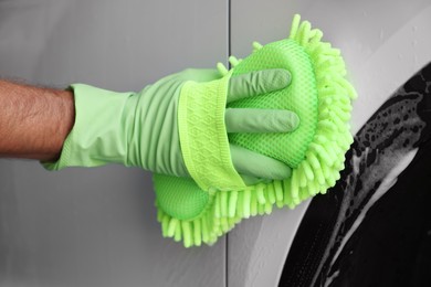 Photo of Worker in rubber gloves washing car with sponge, closeup
