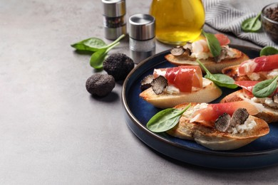 Photo of Delicious bruschettas with cheese, prosciutto and slices of black truffle on light grey table. Space for text