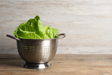 Photo of Colander with fresh leaves of green romaine lettuce on wooden table, space for text