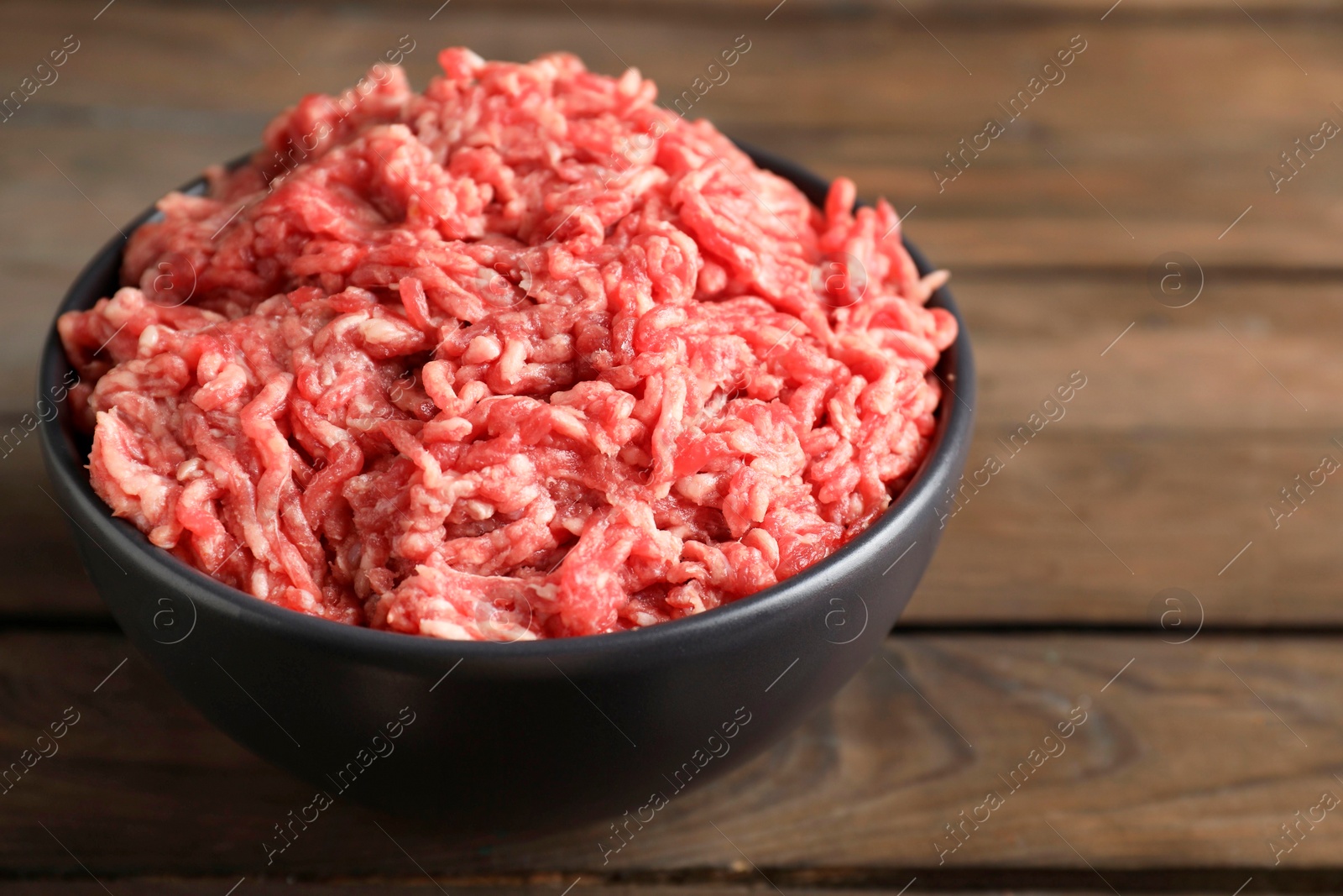 Photo of Raw ground meat in bowl on wooden table, closeup