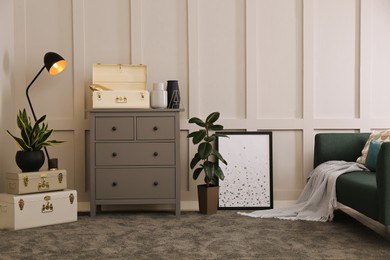 Photo of Stylish room interior with storage trunks, grey chest of drawers and comfortable sofa