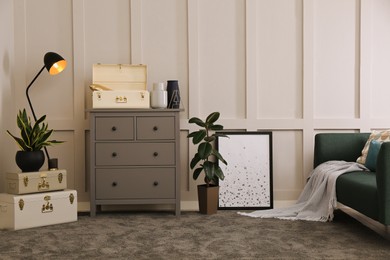 Stylish room interior with storage trunks, grey chest of drawers and comfortable sofa