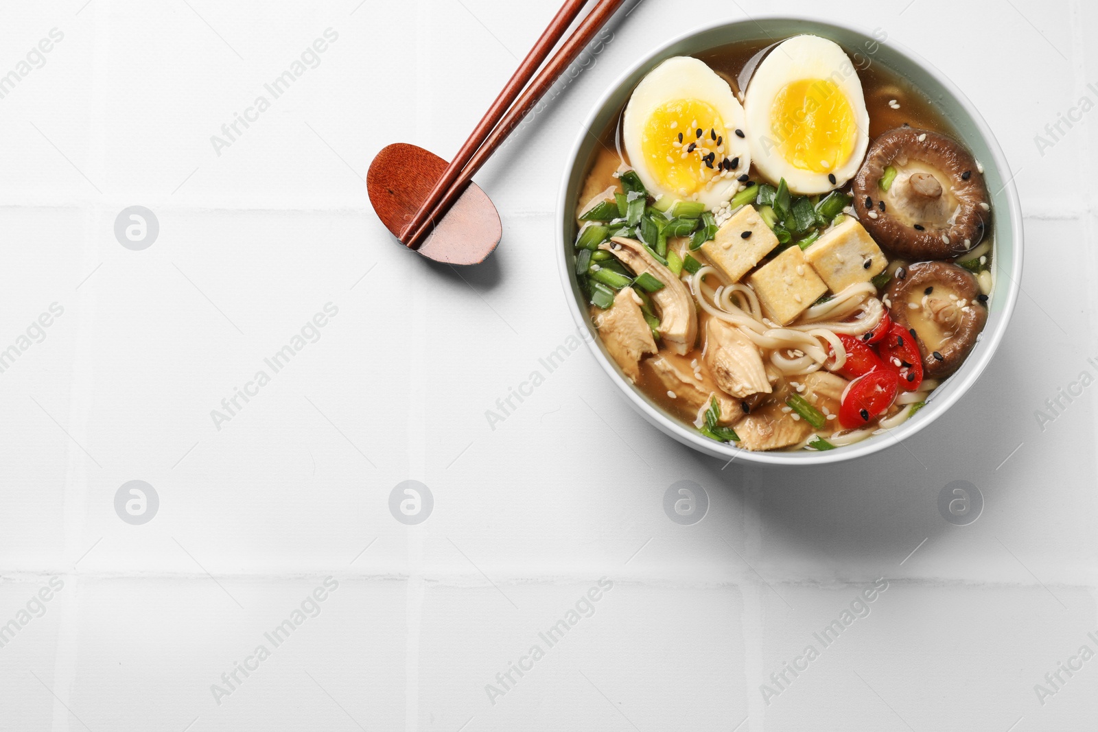 Photo of Noodle soup. Bowl of delicious ramen and chopsticks on white tiled table, top view. Space for text