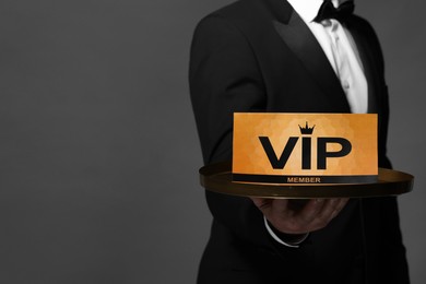 Man holding tray with VIP sign on grey background, closeup. Space for text