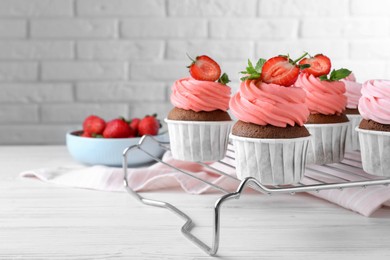 Delicious cupcakes with cream and strawberries on white wooden table. Space for text