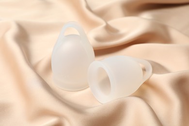 Photo of White menstrual cups on beige silk fabric