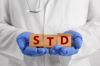 Photo of Doctor holding wooden cubes with abbreviation STD, closeup
