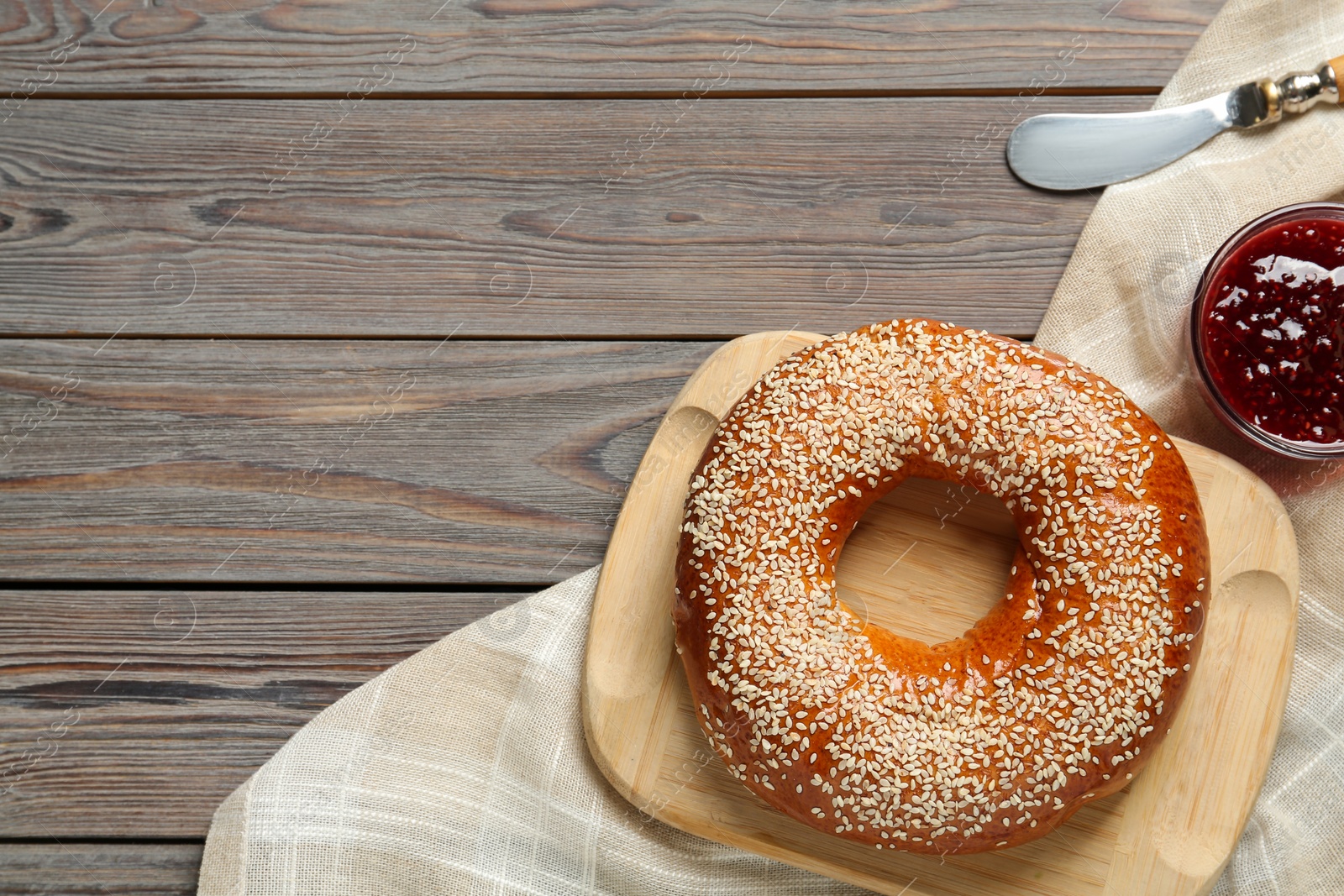 Photo of Delicious fresh bagel with sesame seeds and jam on wooden table, flat lay. Space for text