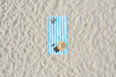 Striped beach towel with straw hat, book, sunglasses and slippers on sand, aerial view