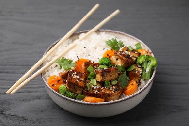 Bowl of rice with fried tofu, broccoli and carrots on grey wooden table, closeup