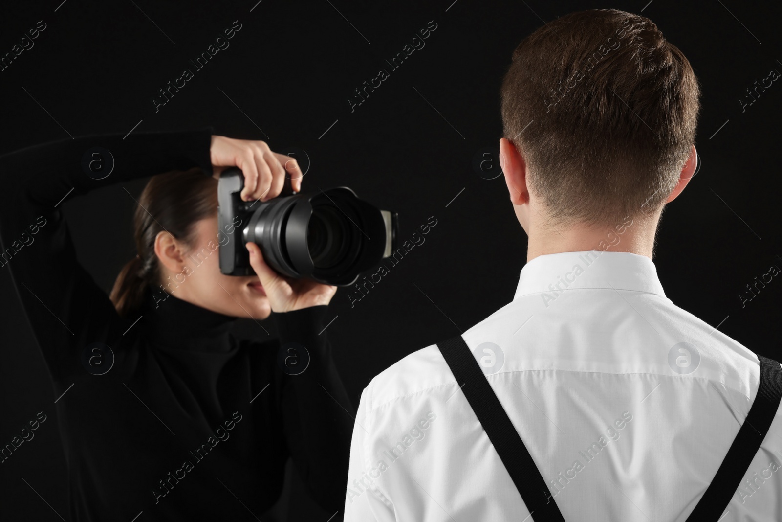 Photo of Professional photographer taking picture of man on black background, selective focus