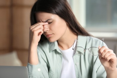 Young woman suffering from eyestrain in office, focus on hand with glasses