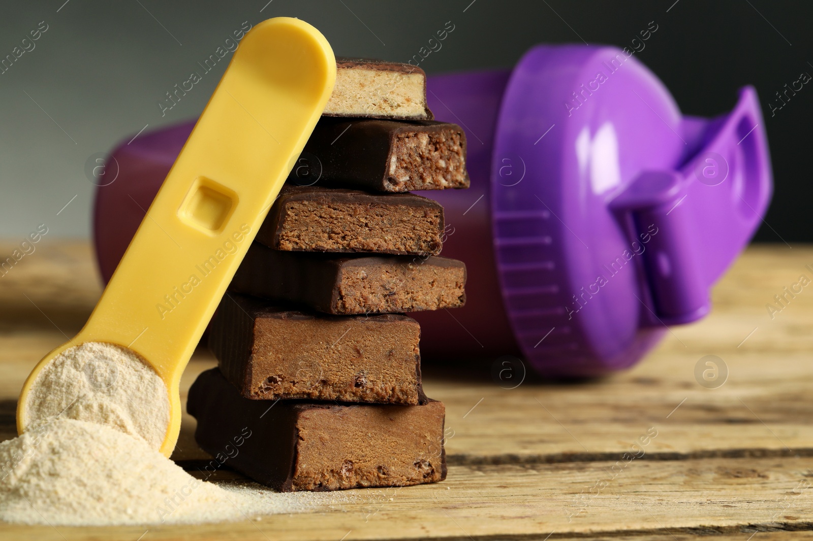 Photo of Different energy bars, protein cocktail and powder on wooden table, closeup