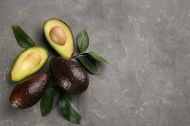 Whole and cut avocados with green leaves on grey table, flat lay. Space for text