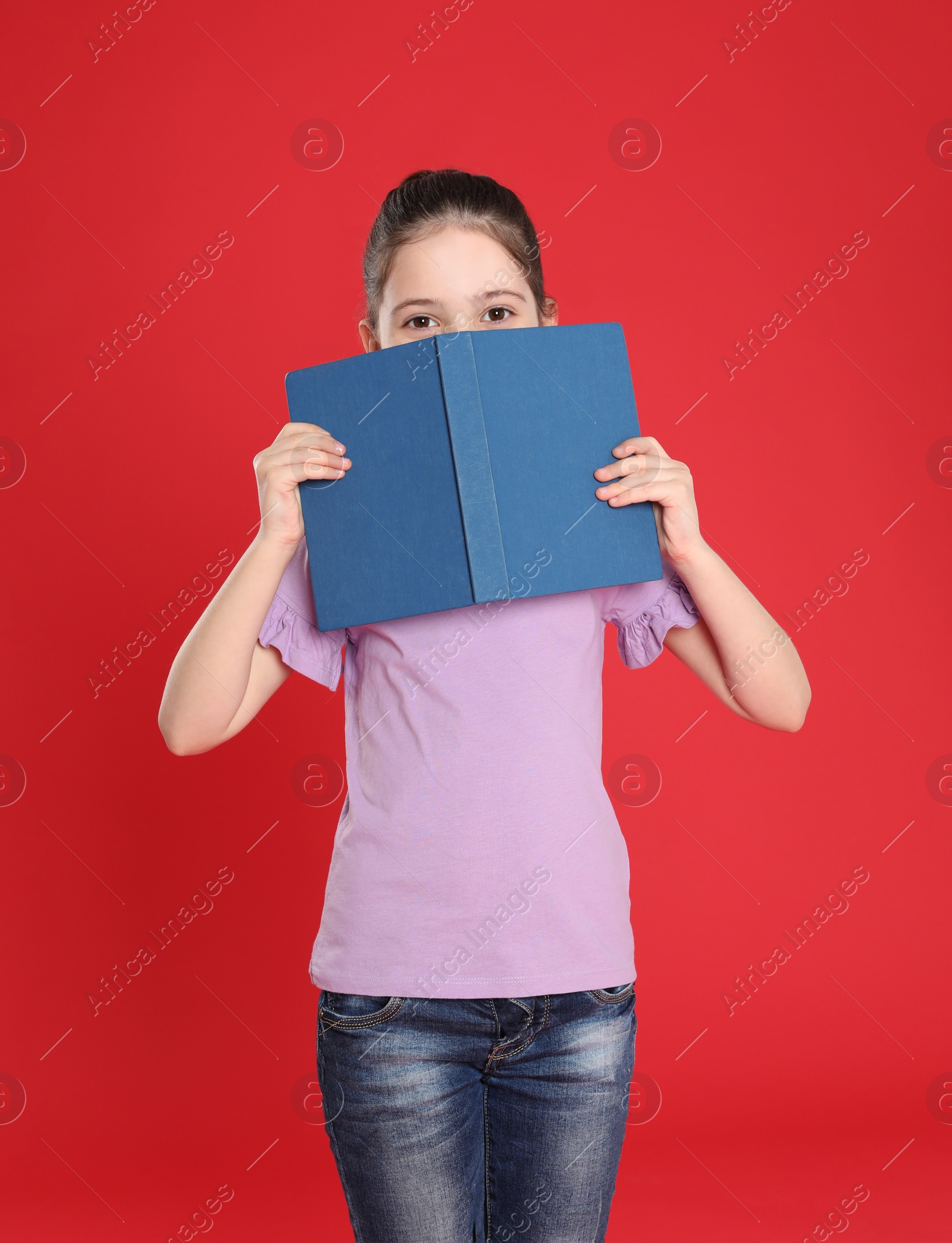 Photo of Cute little girl hiding behind book on color background. Reading activity