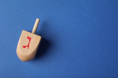 Hanukkah traditional dreidel with letter Gimel on blue background, top view. Space for text