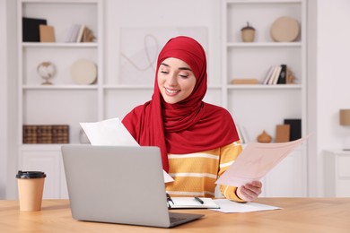 Muslim woman working near laptop at wooden table in room