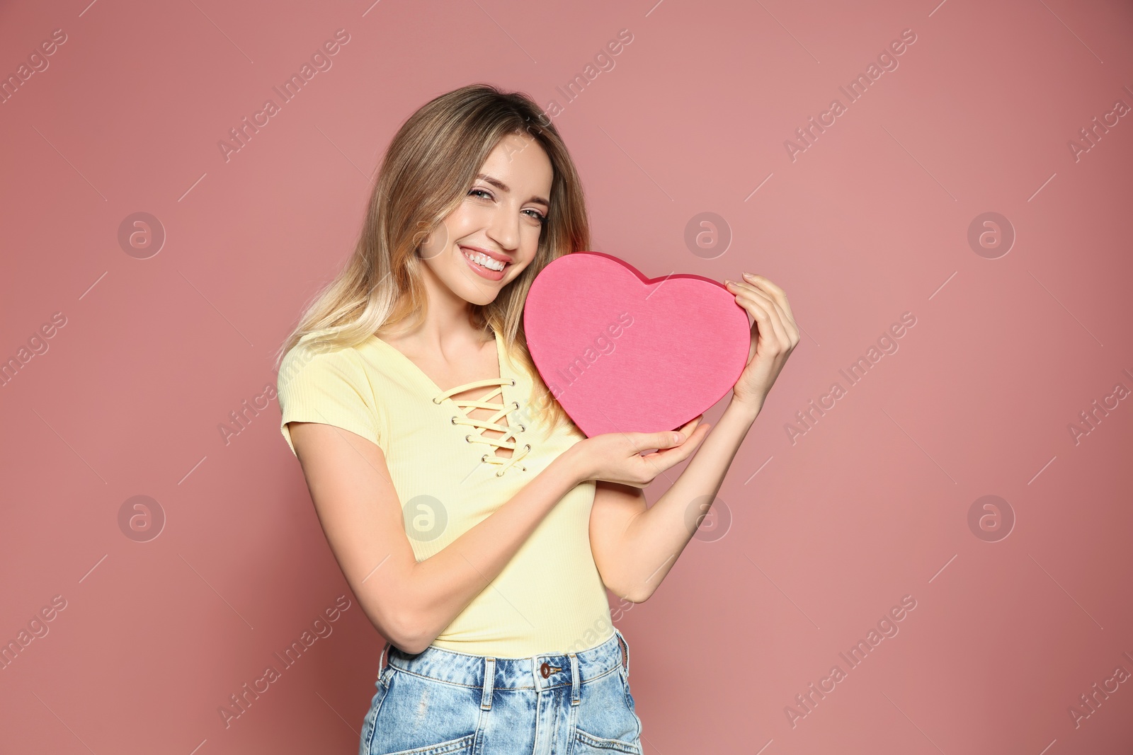 Photo of Portrait of beautiful smiling girl with heart shaped gift box on pink background. International Women's Day