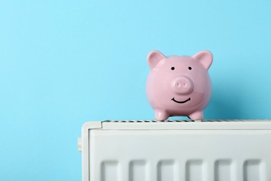 Photo of Piggy bank on heating radiator against light blue background, space for text