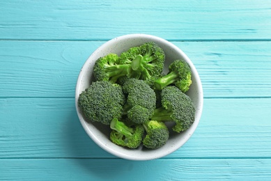 Photo of Bowl of fresh green broccoli on blue wooden table, top view